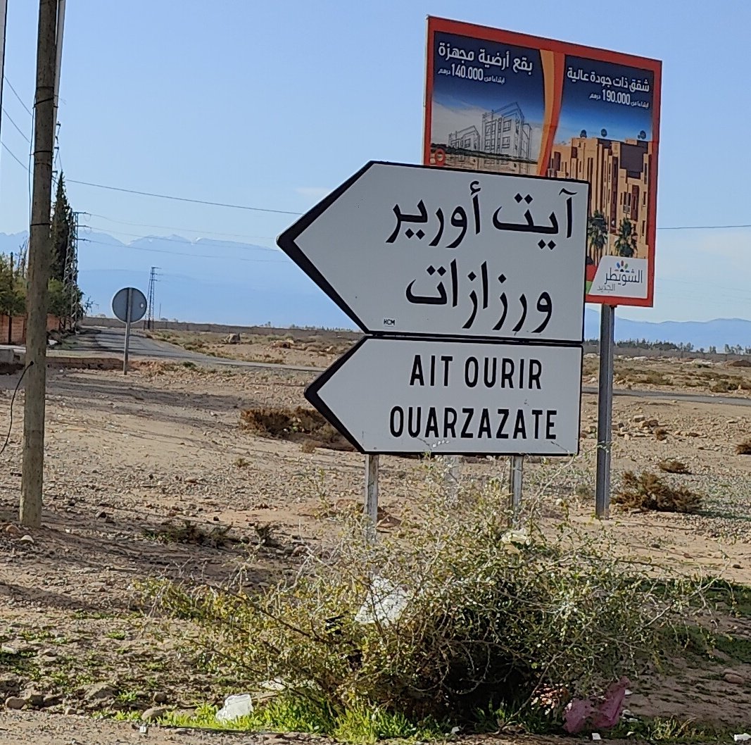 Sign pointing the wat to Ouarzazate with the hight Atlas mountains in the distance.